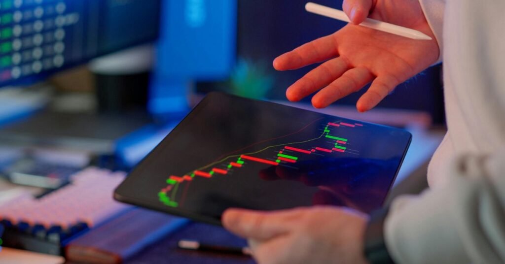 Close-up of a person analyzing a digital trading chart on a tablet showing market trends with green and red candlestick data.